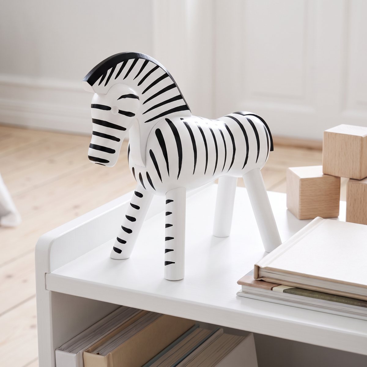 Kay Bojesen Zebra i handmålat bokträ står på en vit hylla i ett barnrum bredvid träklossar och böcker