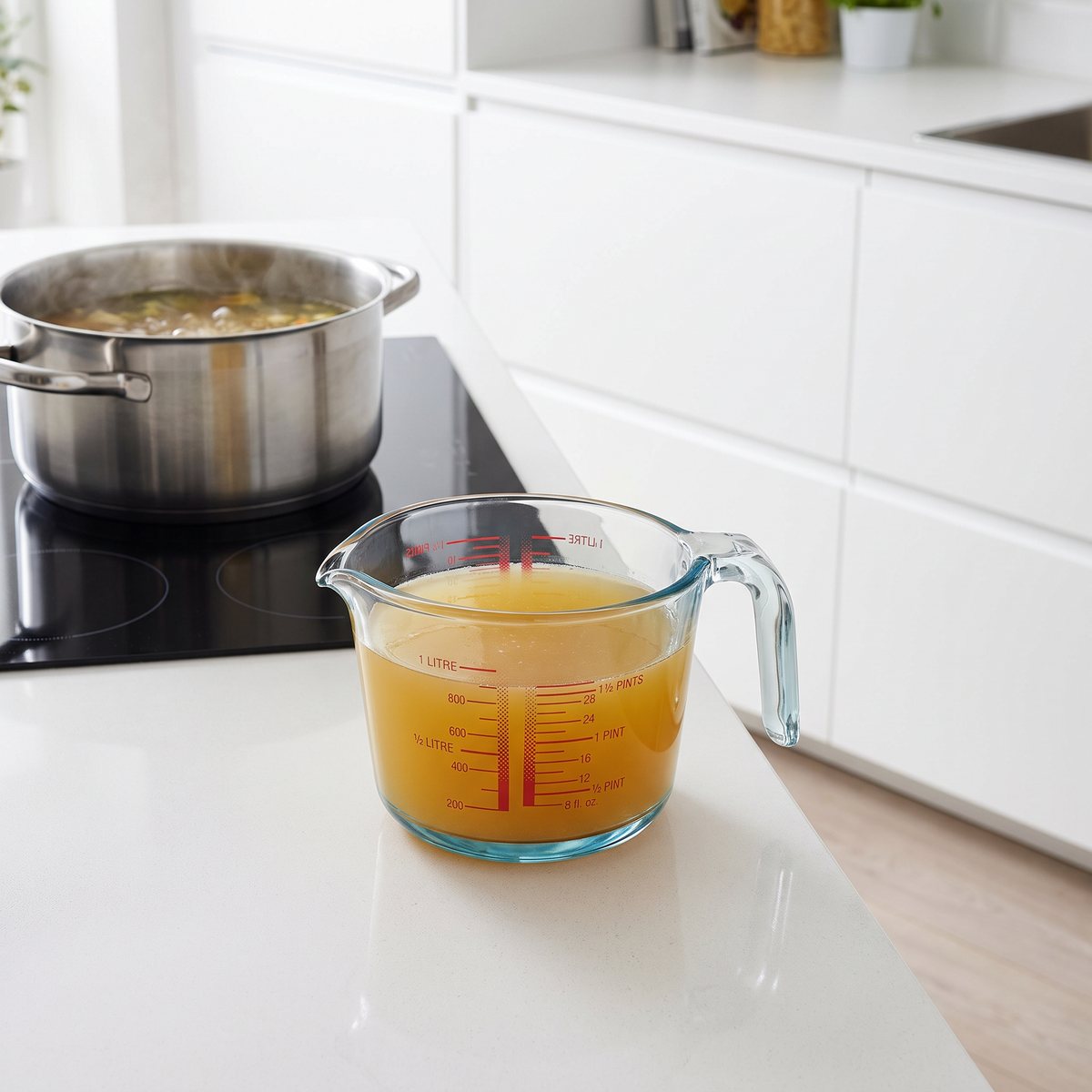 Pyrex måttbägare i glas med varm buljong bredvid en induktionshäll i ett vitt svenskt kök