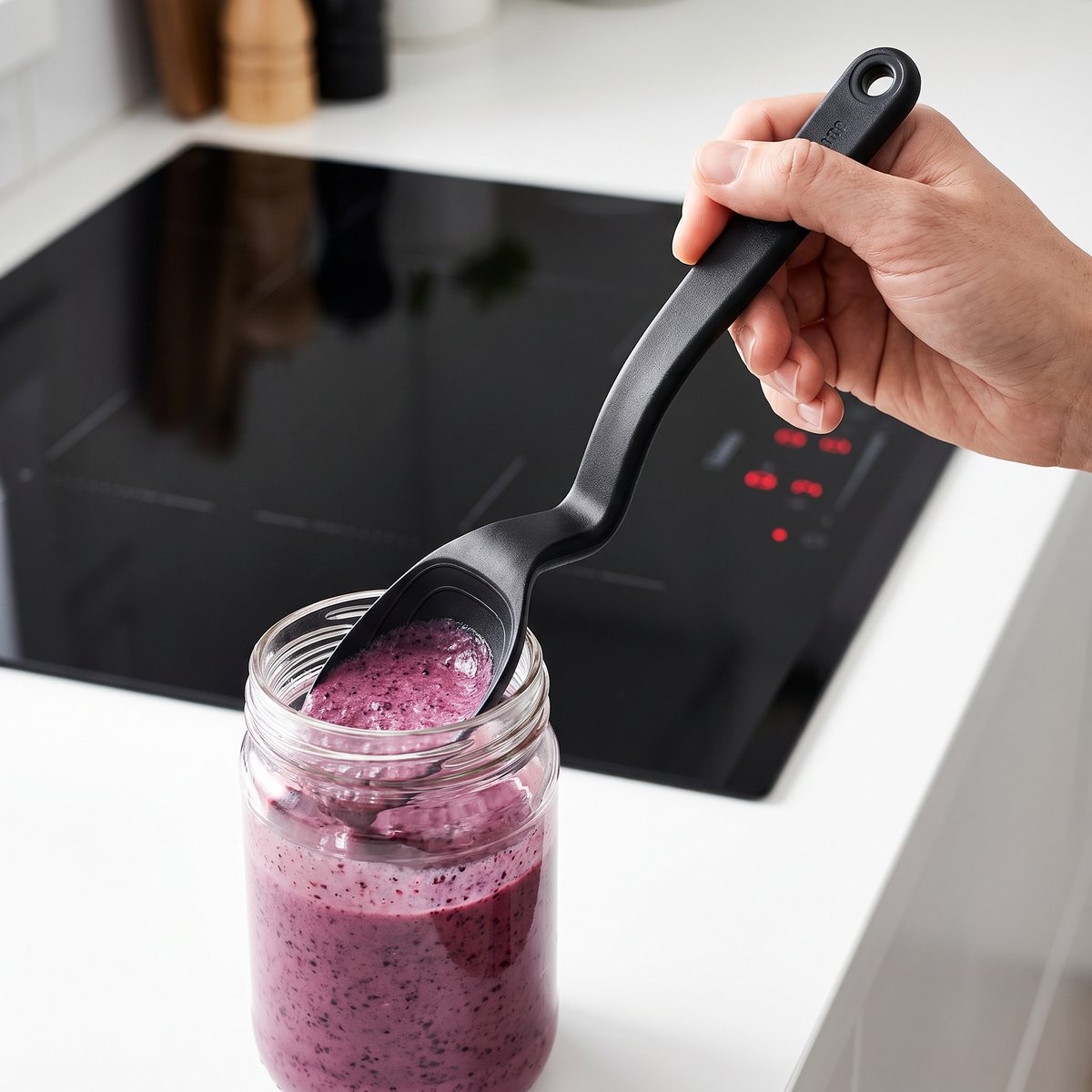 Svart skedformad slickepott som skrapar ur en smoothieburk i ett svenskt kök