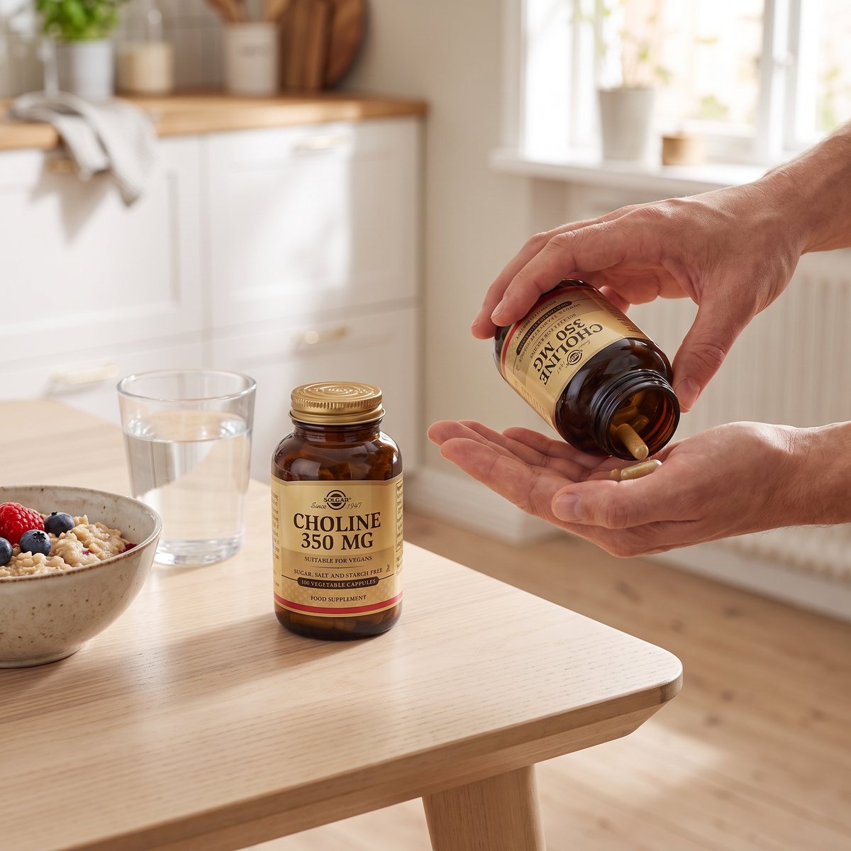 Burk med Solgar Choline 350 mg på ett björkbord i ett svenskt kök vid frukost, med ett glas vatten och en hand som tar fram en kapsel