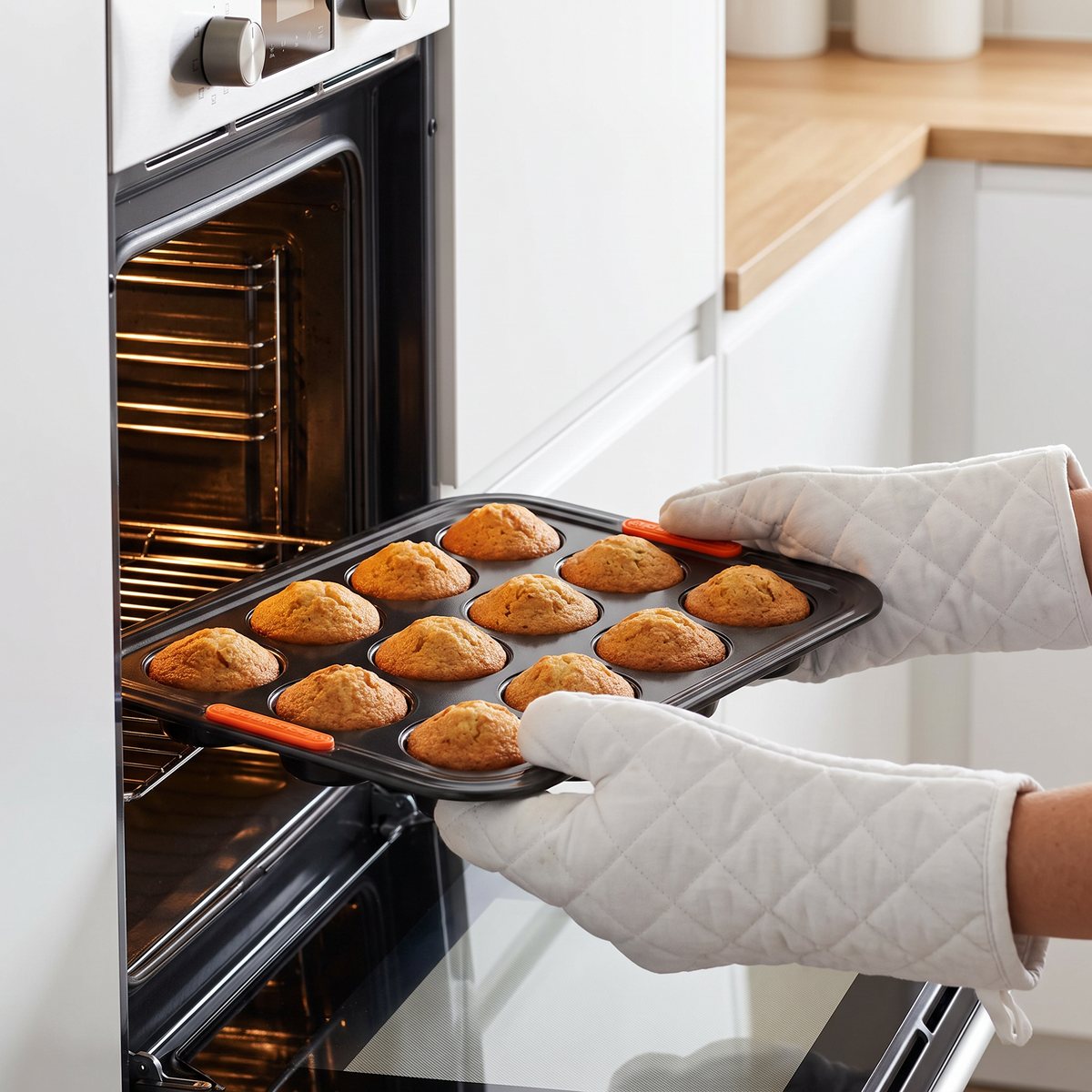 Le Creuset muffinsform med orange silikongrepp lyfts ur ugnen med grytvantar i ett svenskt kök