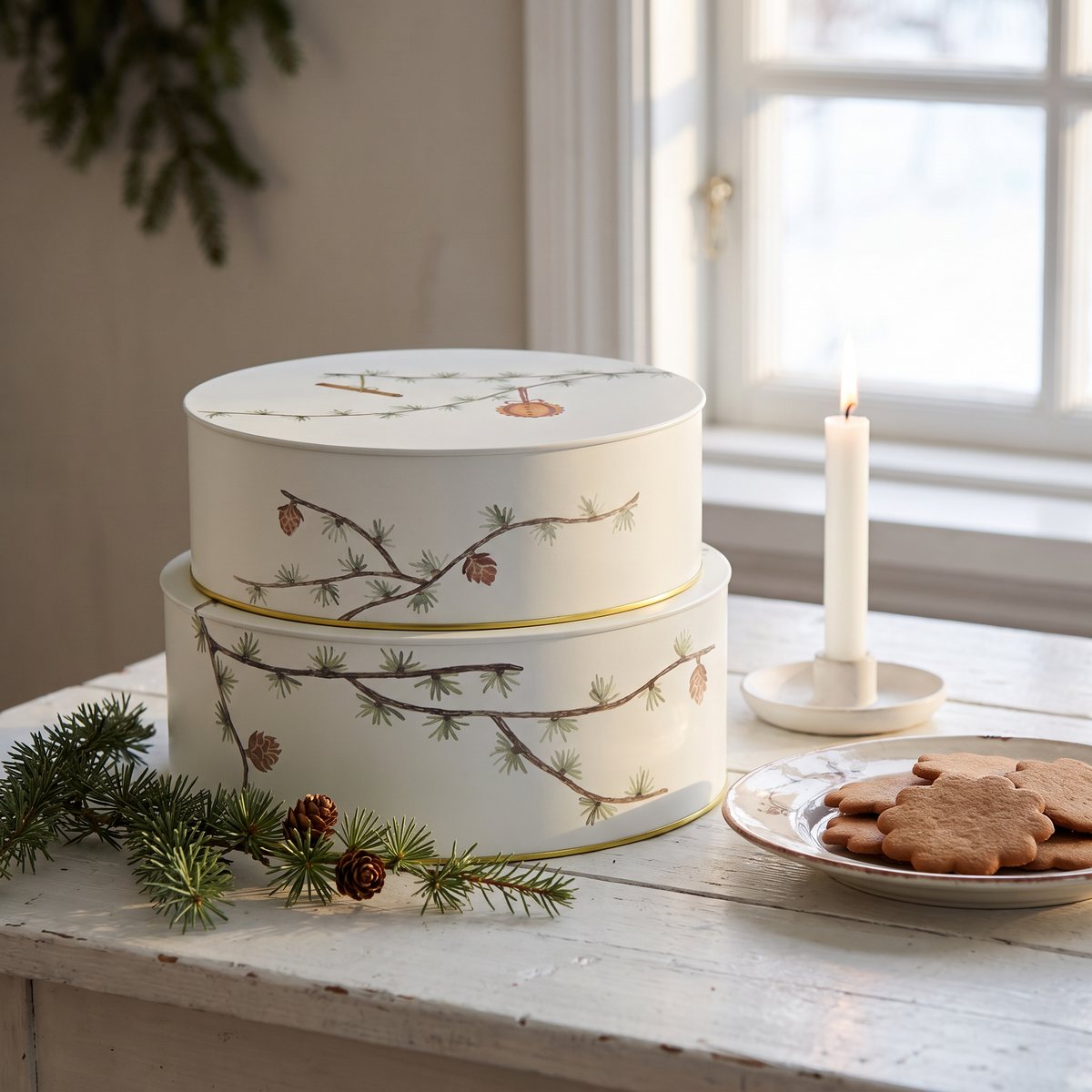 Två vita kakburkar med lärkgrenar och kottar stående på ett vitt trädbord i ett svenskt hem med pepparkakor och ljus
