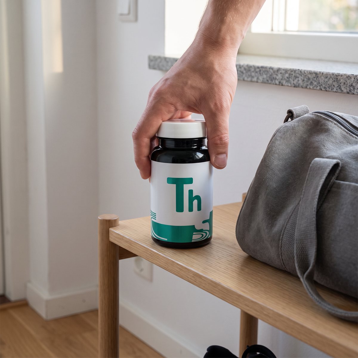 Hand som ställer burken med Strength L-Theanine på en hylla i en svensk hall bredvid en träningsväska