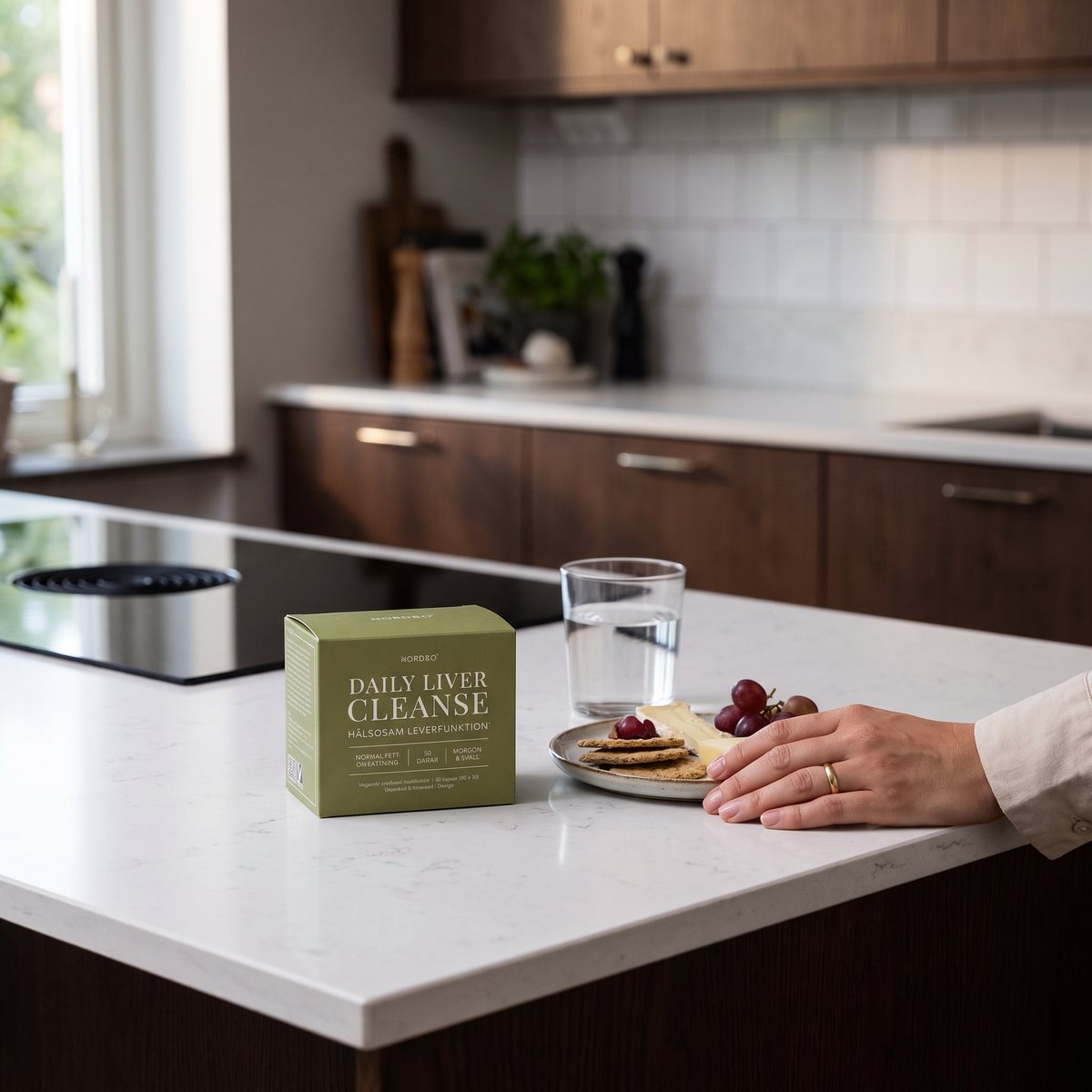 Nordbo Daily Liver Cleanse på en vit bänkskiva i ett svenskt kök med induktionshäll, vattenglas och mellanmål