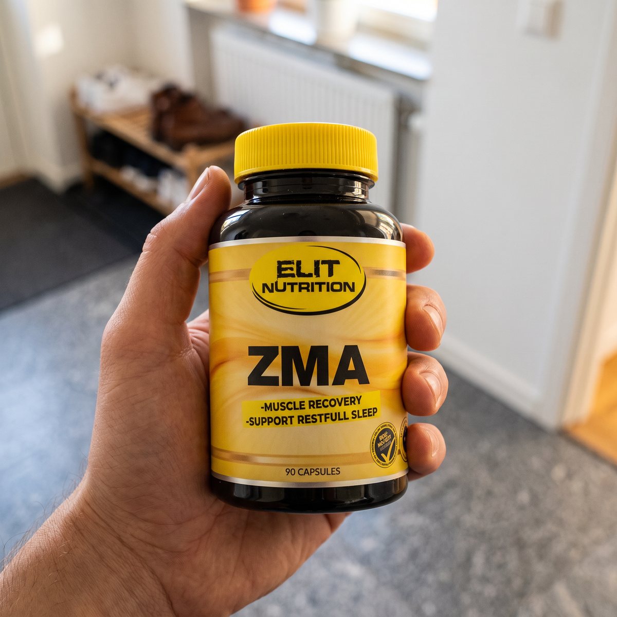 Hand som håller en svart Elit Nutrition ZMA-burk med gult lock i en svensk hall