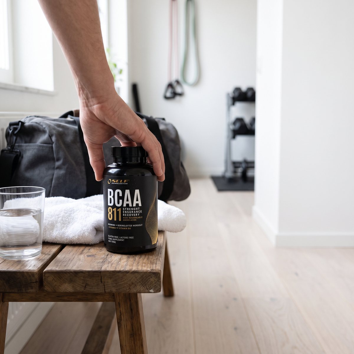 Burk med Self Omninutrition BCAA 8:1:1 på en bänk med handduk och vattenglas i ett svenskt hemmagym