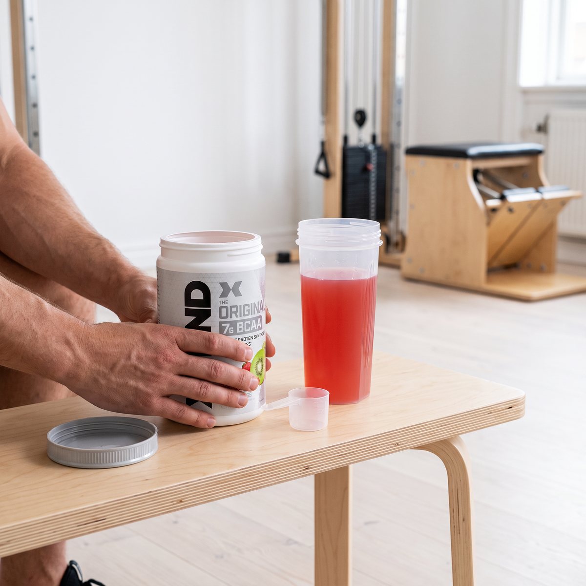 Burk med Scivation Xtend BCAA på en björkbänk i ett svenskt hemmagym med en shaker med rosa dryck bredvid