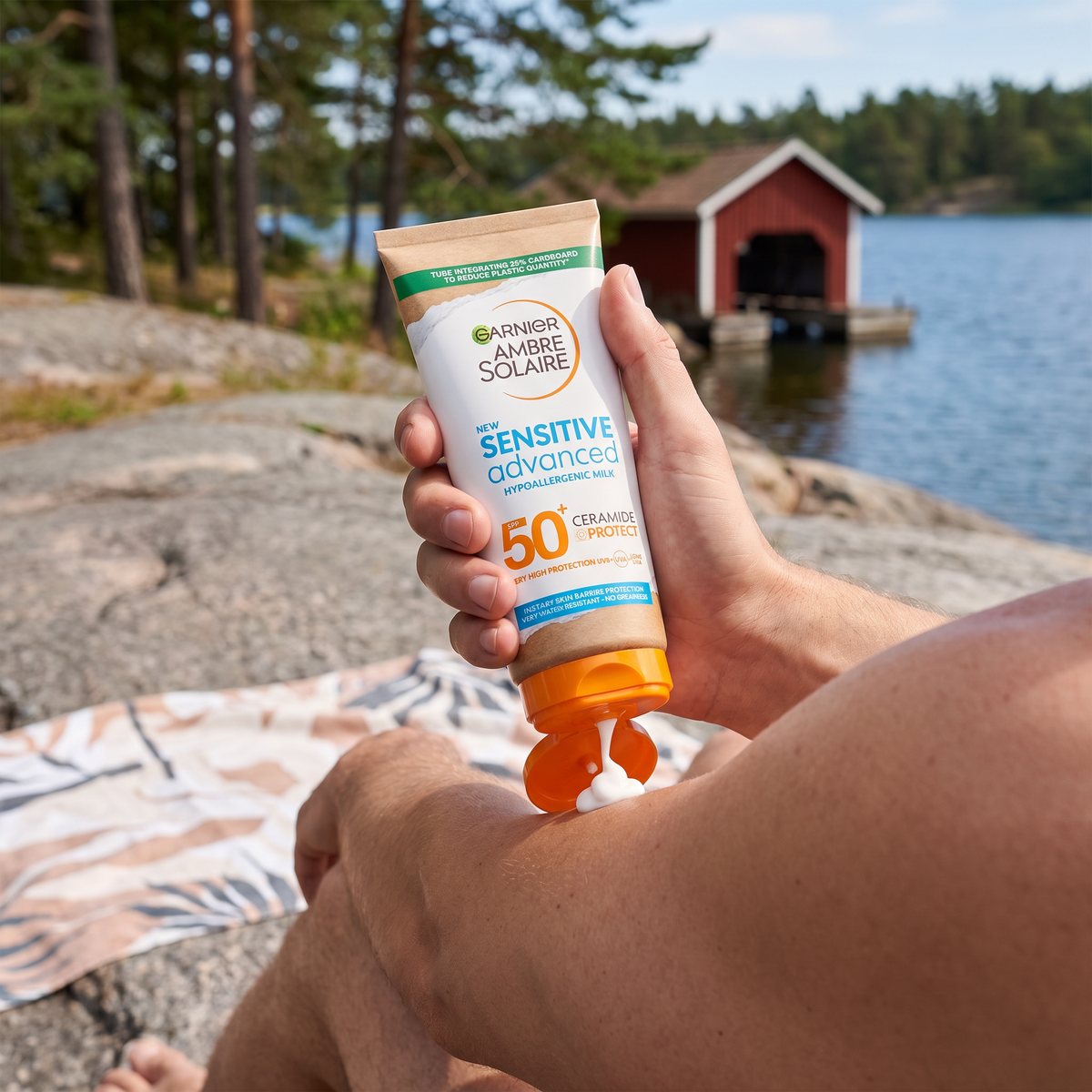 Garnier Ambre Solaire Sensitive Advanced i tub som krams ut på en underarm på en granithäll vid en svensk sjö med rött båthus