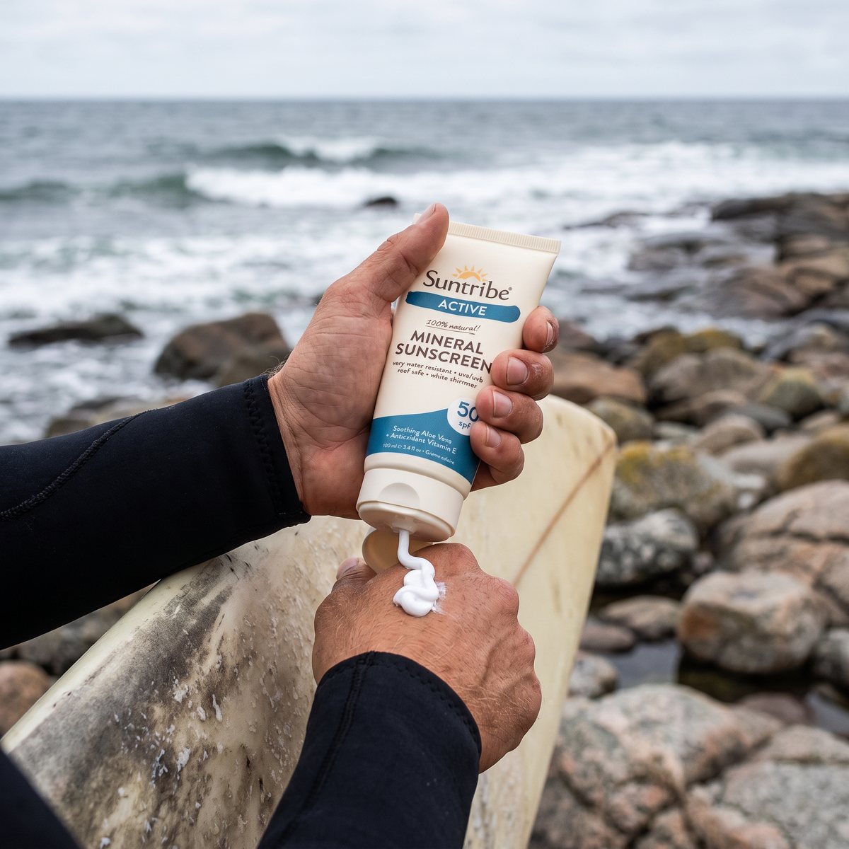 Suntribe Active Mineral Sunscreen som krams ut på handen vid en surfbräda på klippig svensk västkust