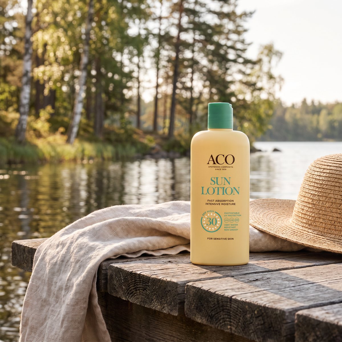 ACO Sun Lotion på en träbrygga vid en svensk skogssjö med linnehandduk och solhatt