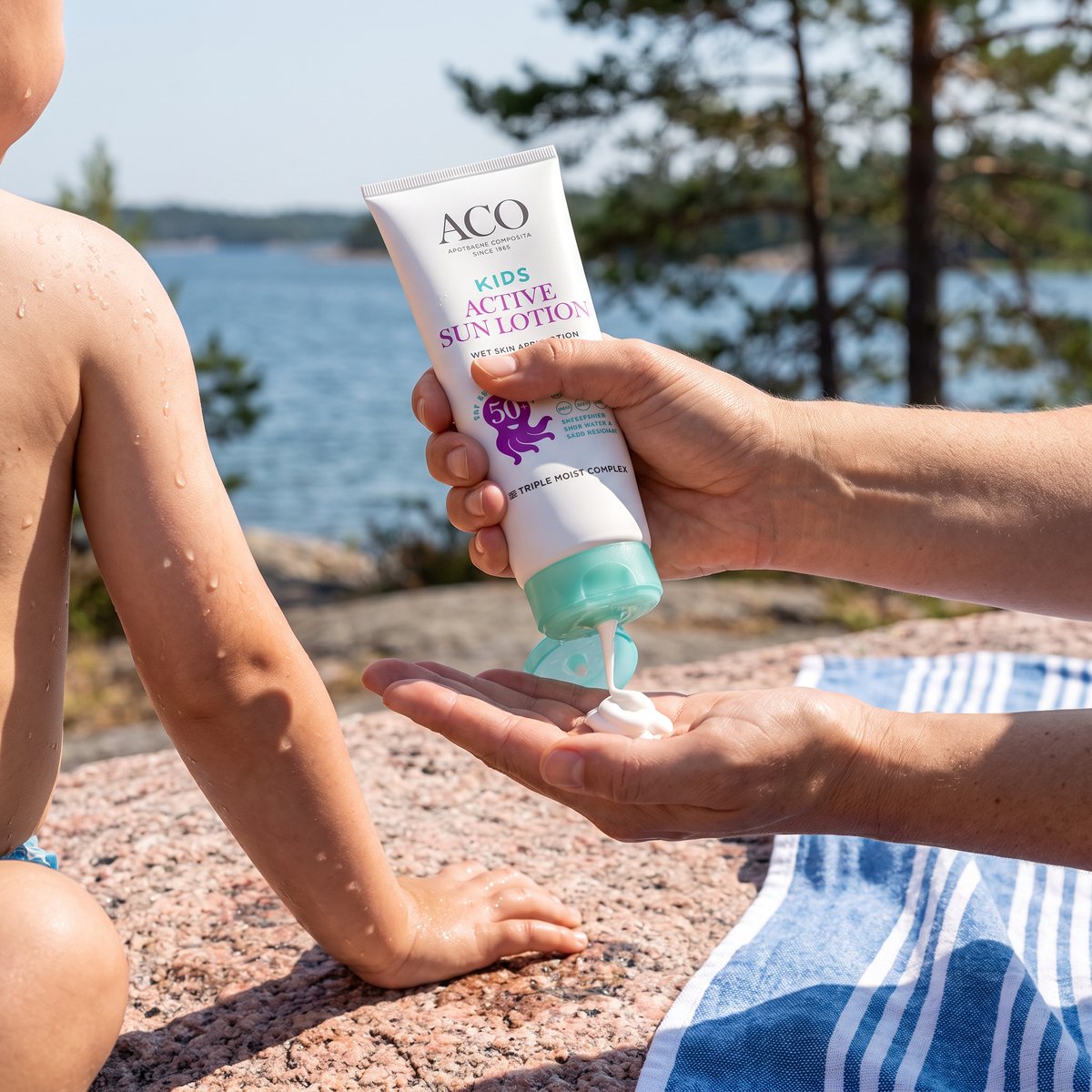 ACO Sun Kids Lotion pressas ut i handen bredvid ett badblött barn på en granithäll i skärgården