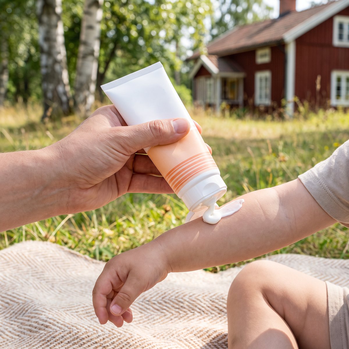 Bioregena Sunscreen Cream Kids trycks ut på ett barns underarm på en filt i en svensk sommaräng