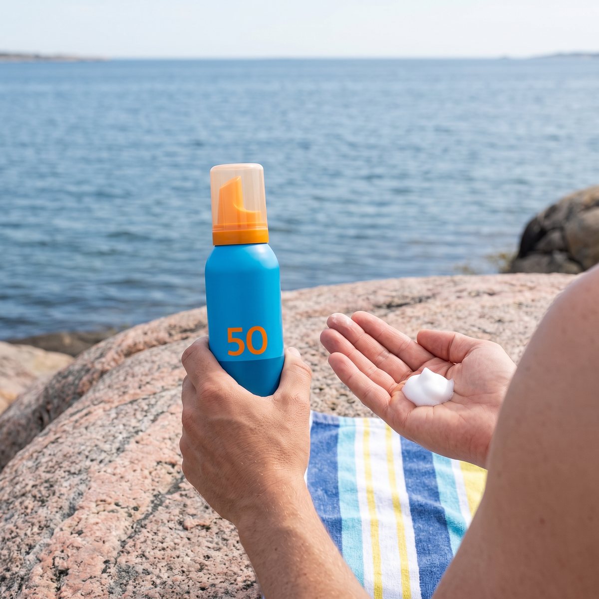 EVY Sunscreen Mousse SPF 50 hålls i handen med en klick vitt skum i andra handflatan, på en granitklippa i skärgården vid havet
