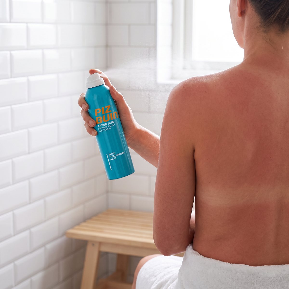 Piz Buin After Sun Instant Relief Mist Spray sprayas mot axeln i ett vitkaklat badrum efter duschen