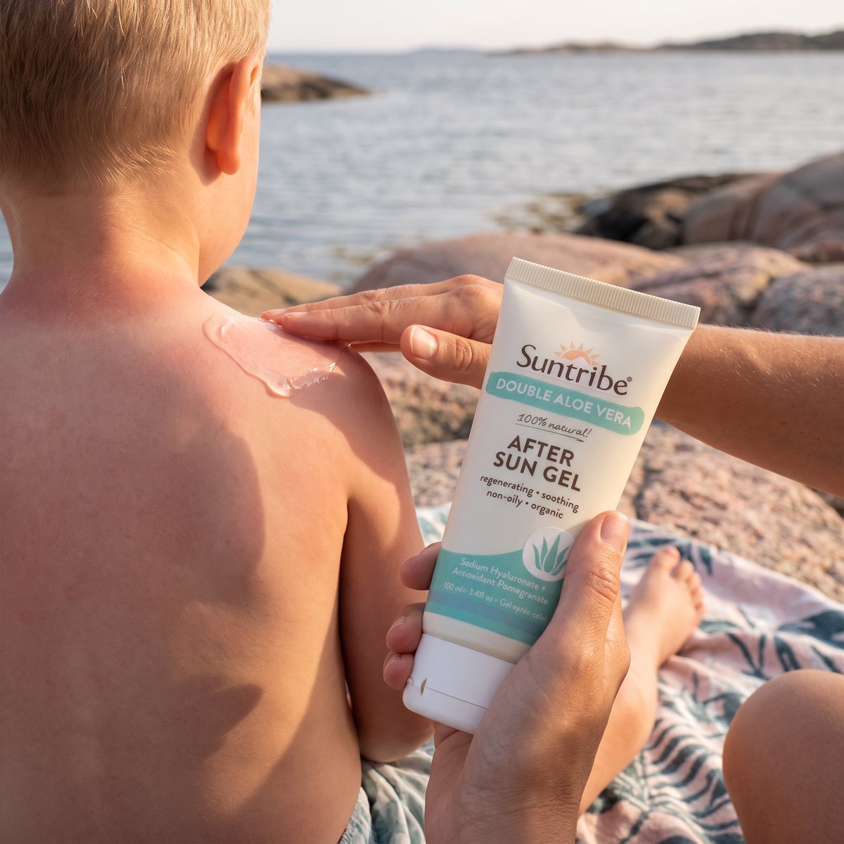 Vuxen smörjer Suntribe After Sun Gel på ett barns solvarma axel på klipporna vid västkusten