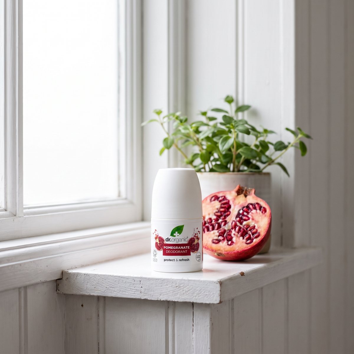 Dr Organic Deodorant Granatäpple på en hylla vid fönstret i ett svenskt badrum bredvid en granatäpplehalva