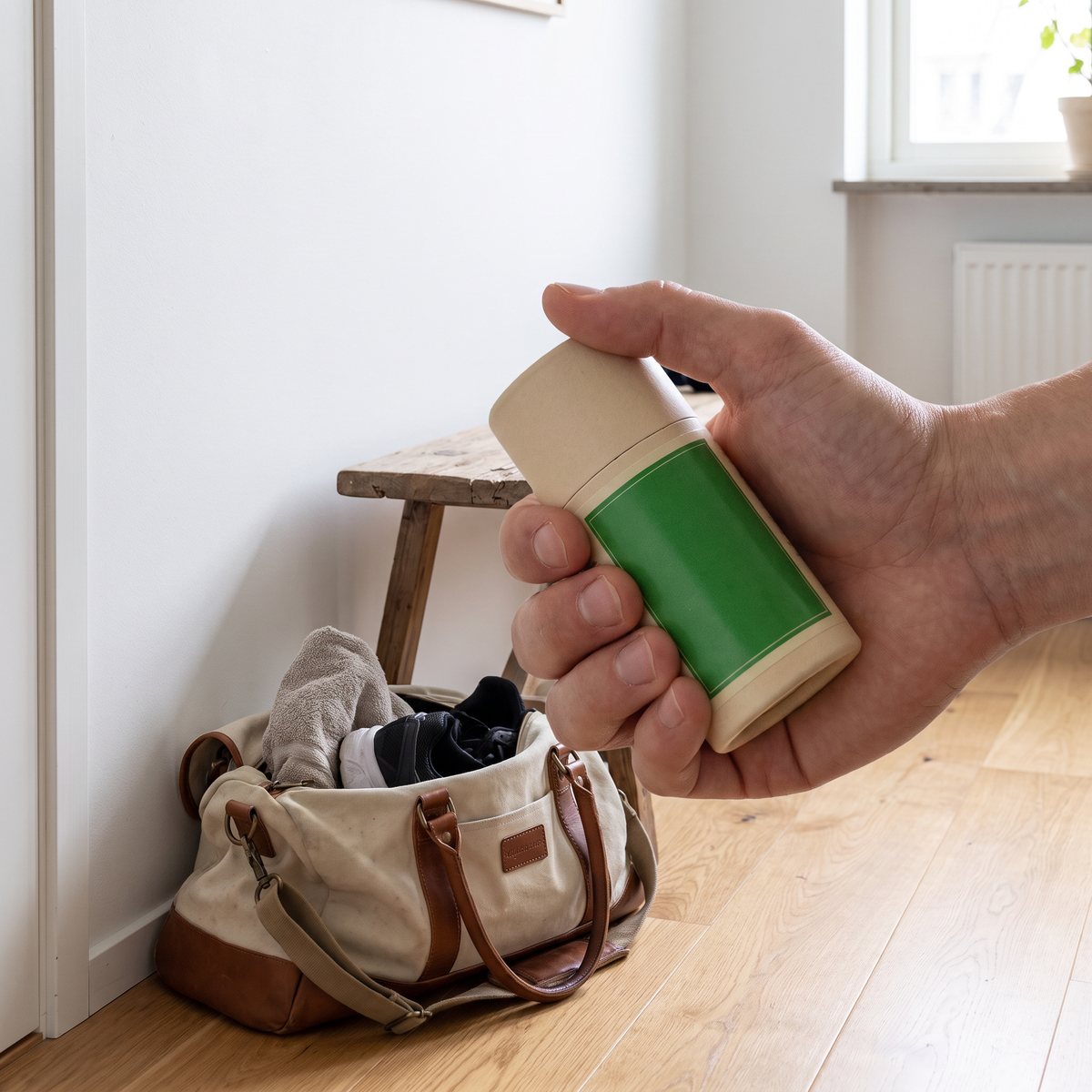 Alepeo deodorantstick i kartongtub hålls i handen intill en träningsväska i en svensk hall