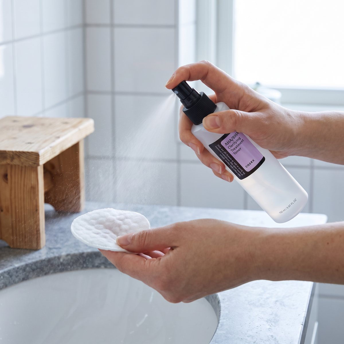 COSRX AHA/BHA Clarifying Treatment Toner sprayas på en bomullsrondell över ett handfat i ett svenskt badrum