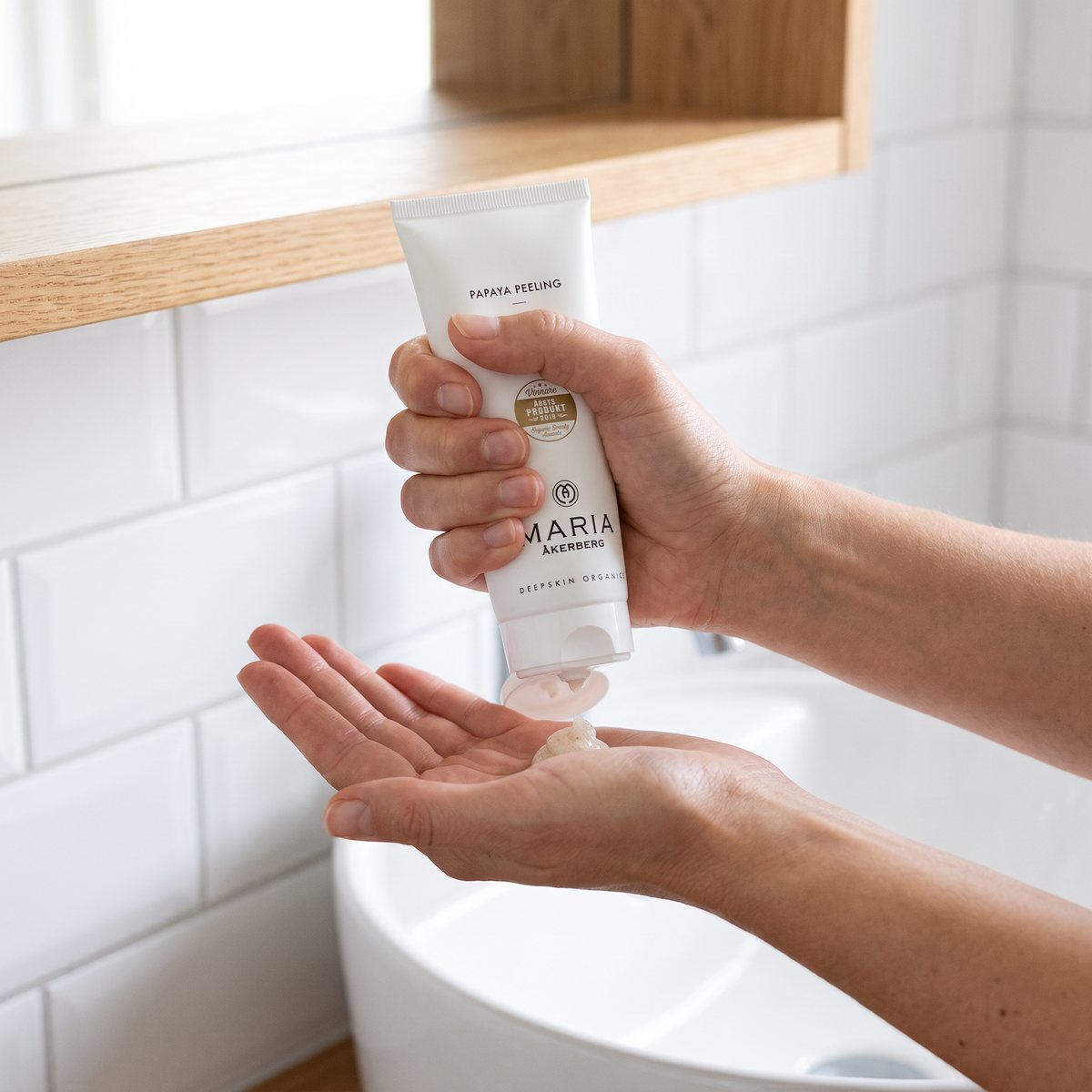 Maria Åkerberg Papaya Peeling i vit tub, en klick peeling pressas ut i handen i ett ljust svenskt badrum