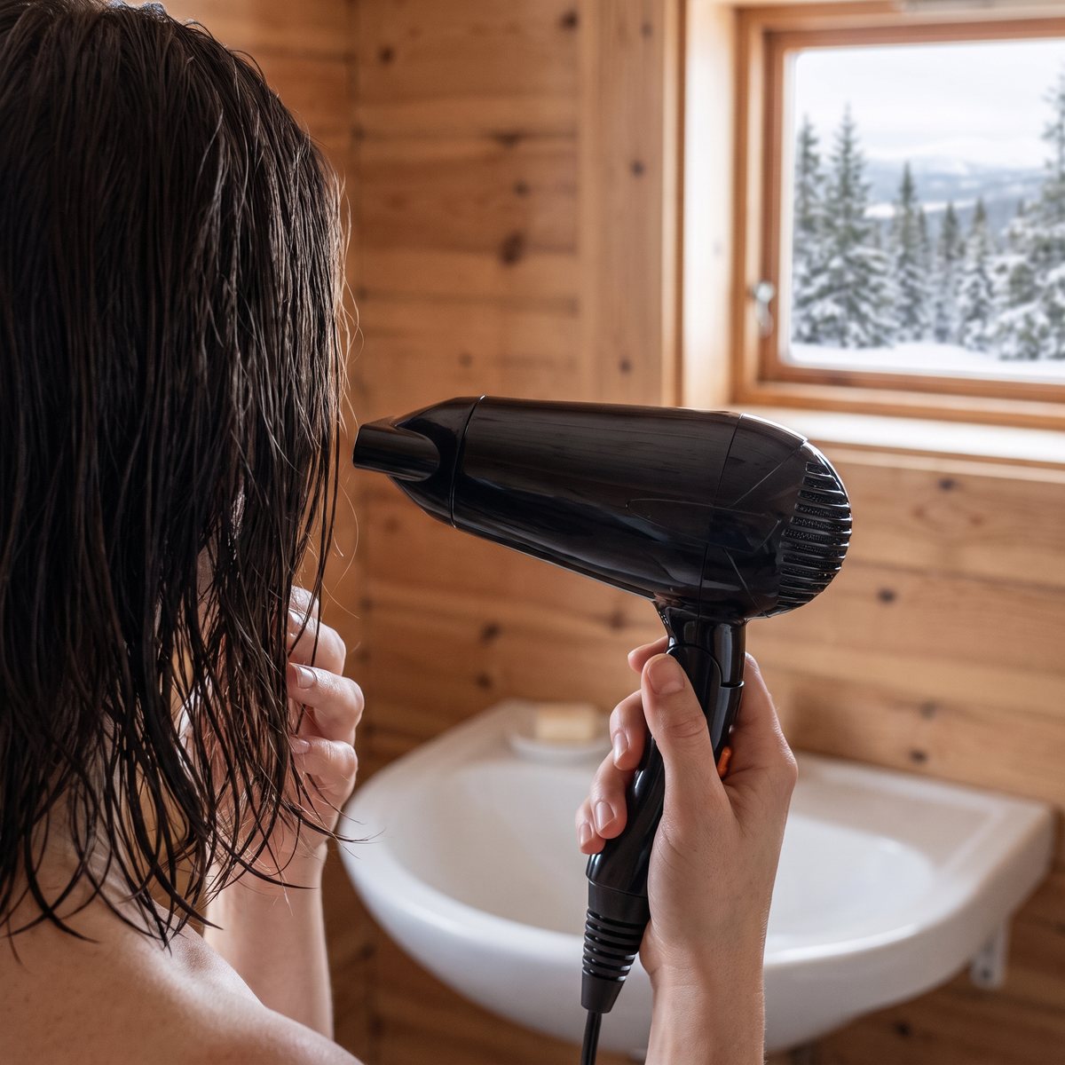 BaByliss Travel Dry 2000, en svart resefön, torkar mörkt hår i ett fjällstugebadrum med träpanel och snöig granskog utanför fönstret