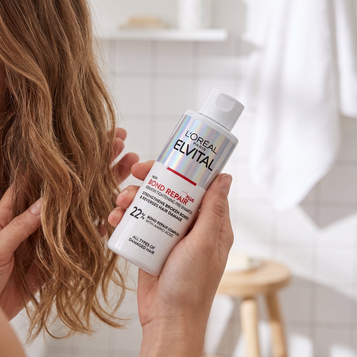L'Oréal Paris Elvital Bond Repair Pre-Shampoo hålls i handen medan produkten arbetas in i håret i ett svenskt badrum