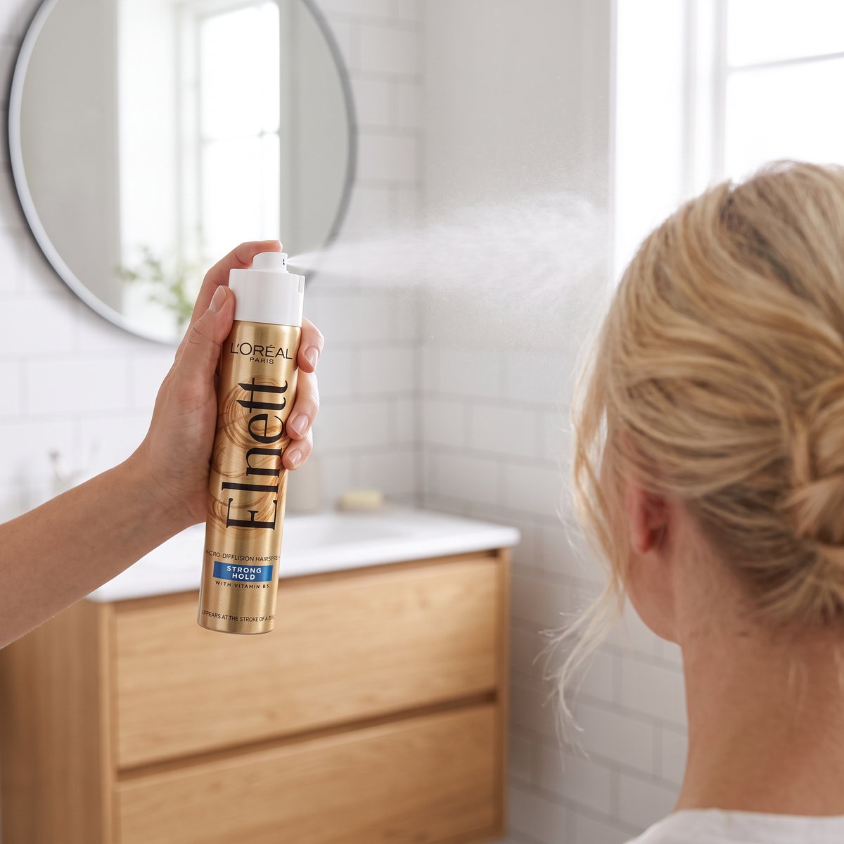 L'Oréal Paris Elnett Strong sprayas över en uppsättning blont hår i ett svenskt badrum med vita kakelväggar
