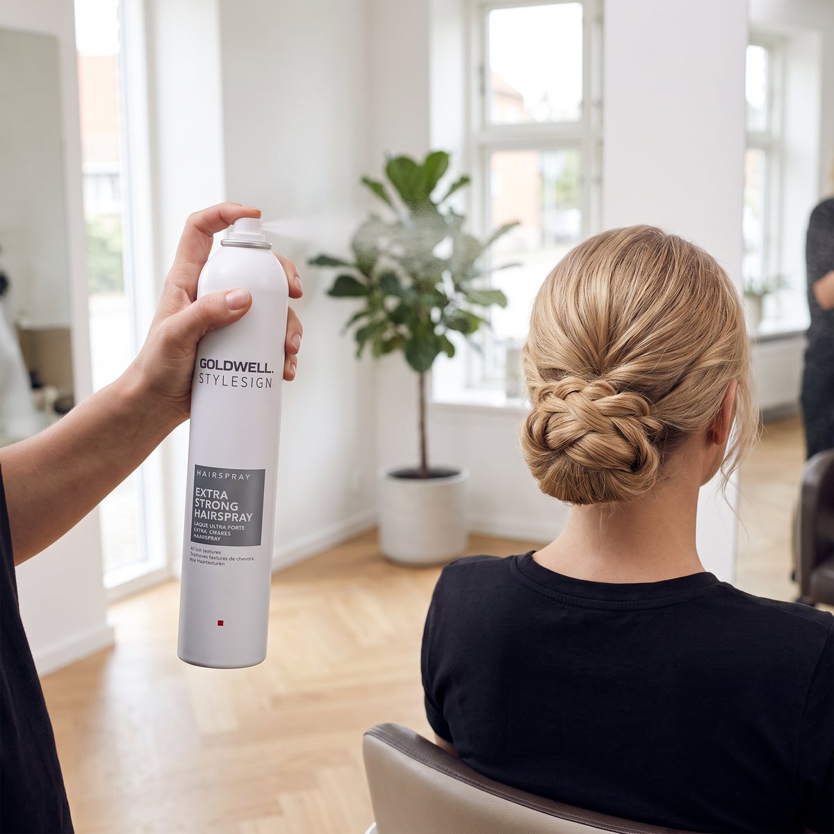 Goldwell StyleSign Extra Strong sprayas över en uppsättning hos en frisör i en ljus salong