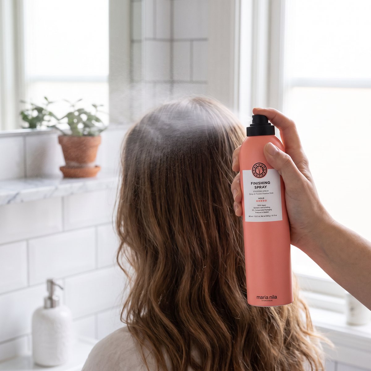 Maria Nila Finishing Spray sprayas över långt vågigt hår i ett ljust svenskt badrum