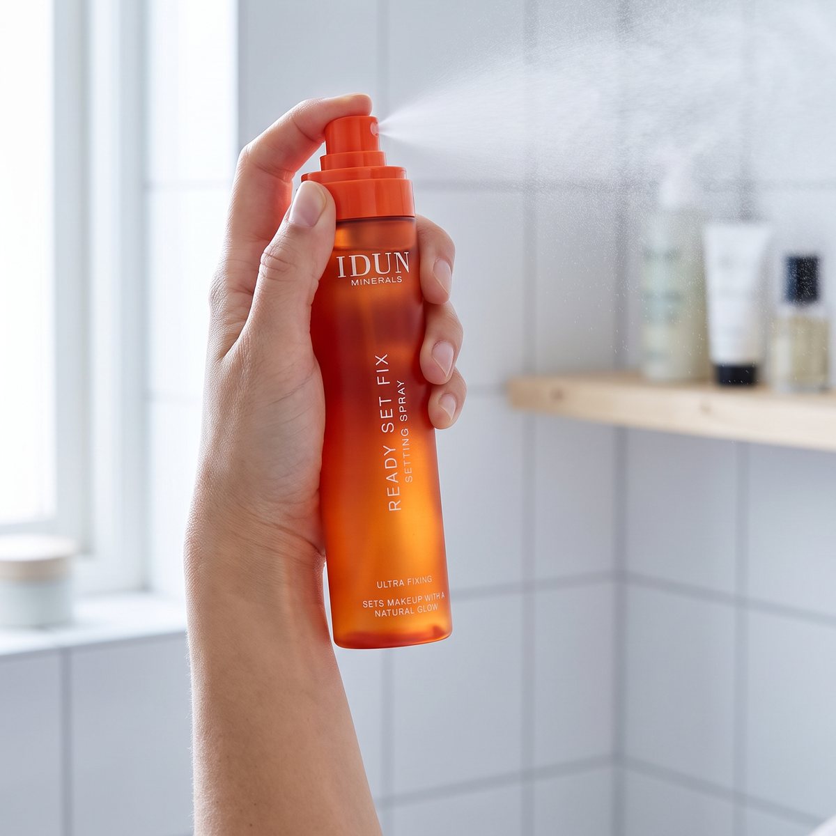 Hand som sprayar IDUN Minerals Ready Set Fix i ett ljust badrum med vitt kakel och hylla i ljust trä