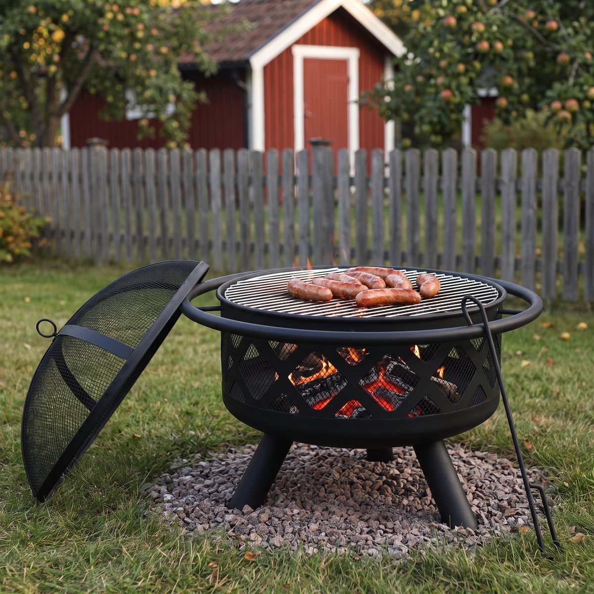 Habanero Eldsland med korv på grillgallret, locket med gnistskydd bredvid och eldgaffeln lutad mot korgen på en svensk gräsmatta