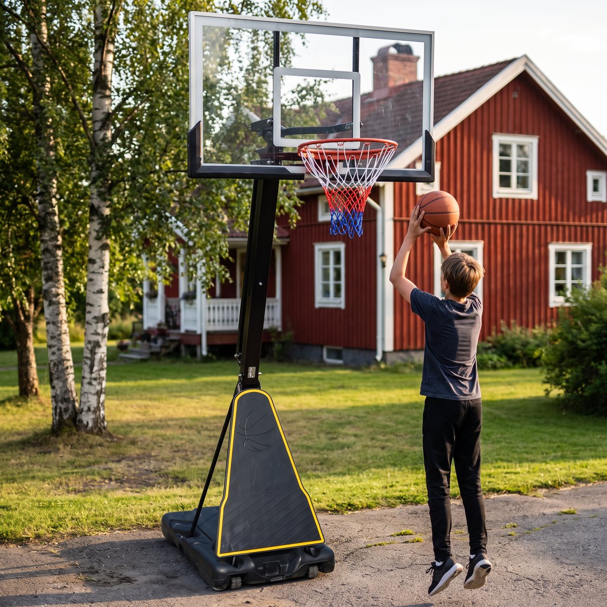 Bedly Pro Court 305 på en asfalterad uppfart framför en röd trävilla med björkar, där en tonåring skjuter mot korgen.