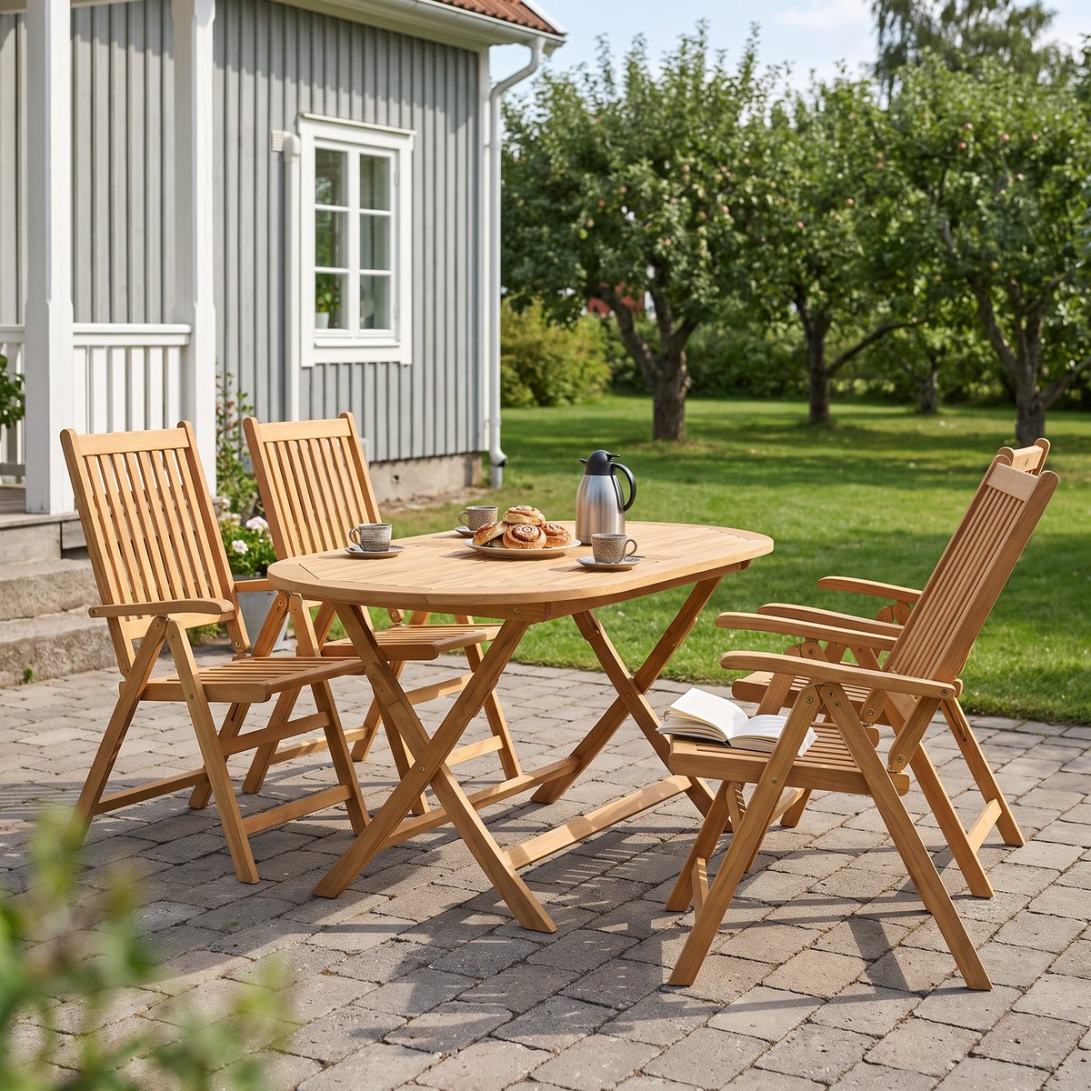 vidaXL matgrupp i massiv teak med fyra positionsstolar, en stol bakåtlutad med en bok på sitsen, på en stenlagd uteplats vid ett grått svenskt trähus.