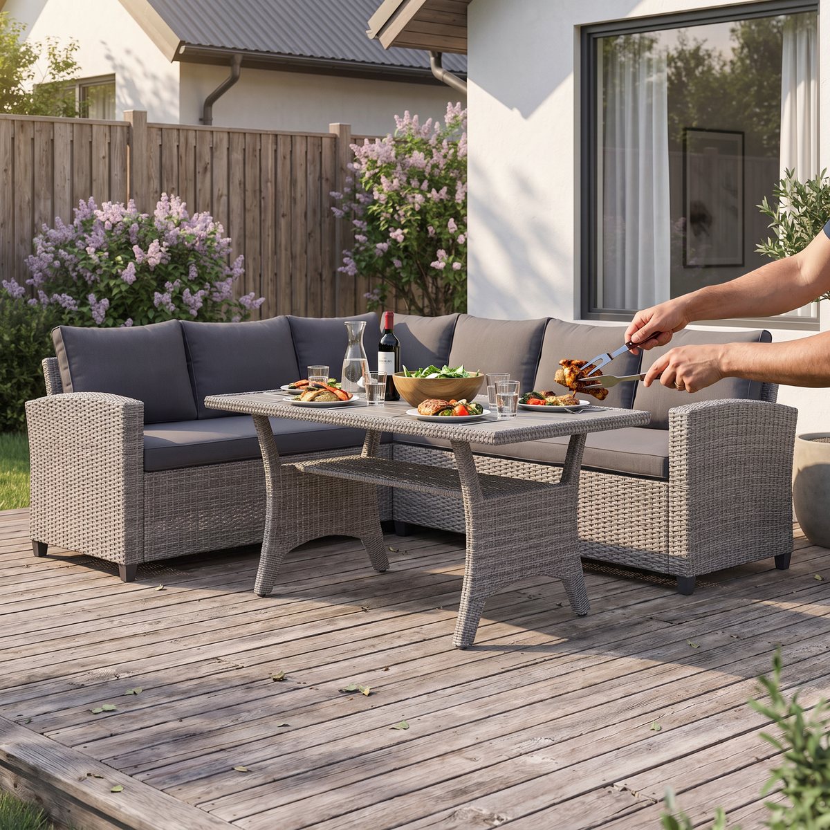 Grå hörnsoffa i konstrotting med högt matbord dukat för grillmiddag på trätrall vid en vit svensk villa