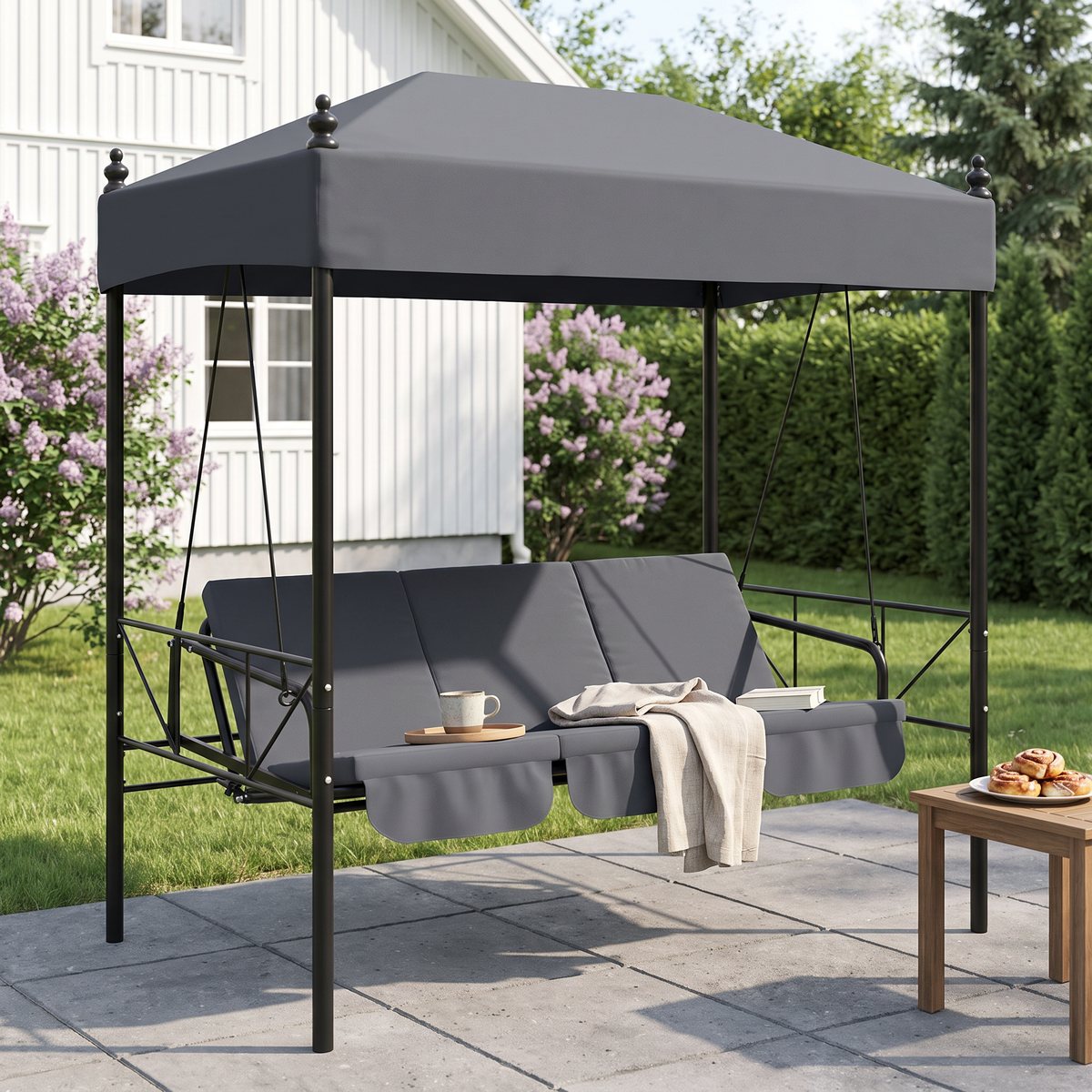 Mörkgrå vidaXL-hammock med fast tak och tre kuddar på en stenlagd uteplats vid en vit svensk villa med syrener