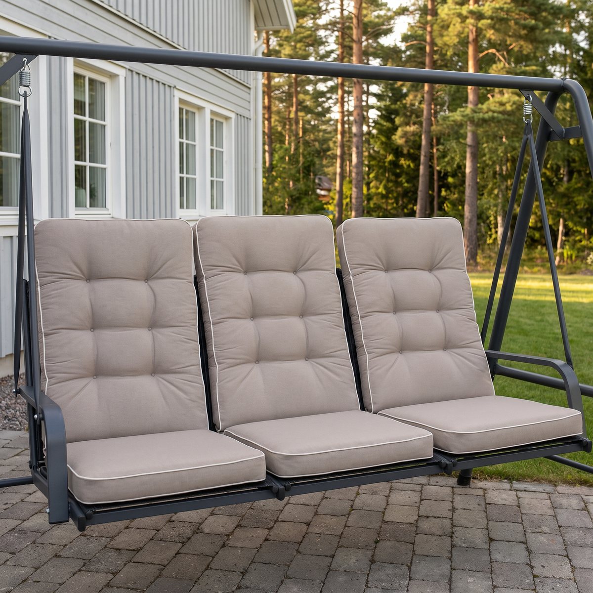 Tre beigea panamadynor med hög rygg, en per sittplats, i en hammock på en stenlagd uteplats vid en grå villa med tallskog