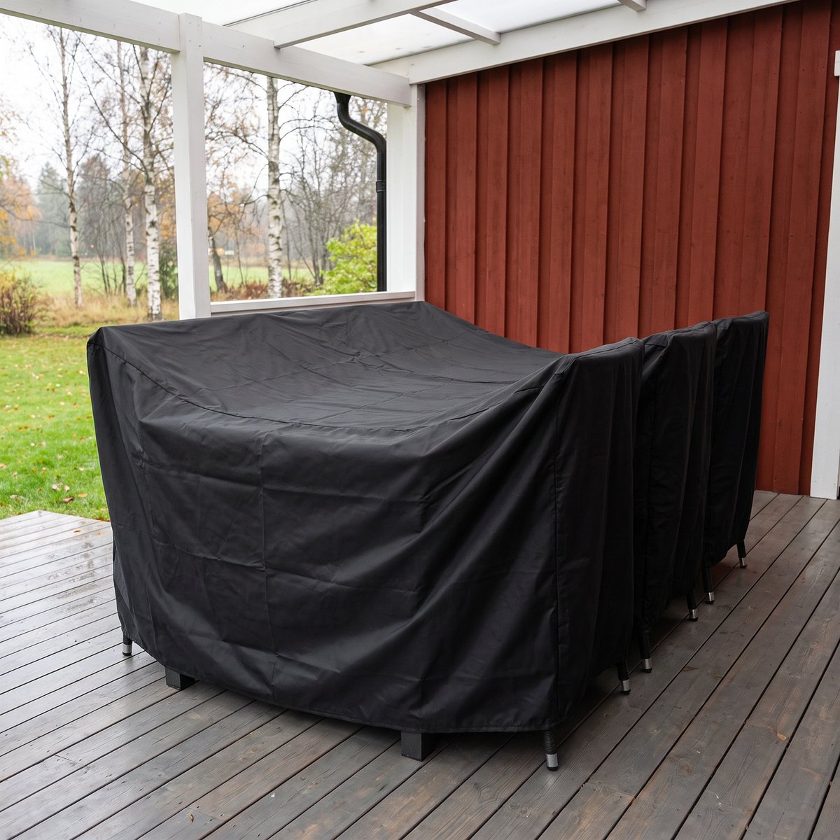 Svart Lyfco-skyddsöverdrag över en matgrupp med stolar på en altan under tak vid ett rött trähus