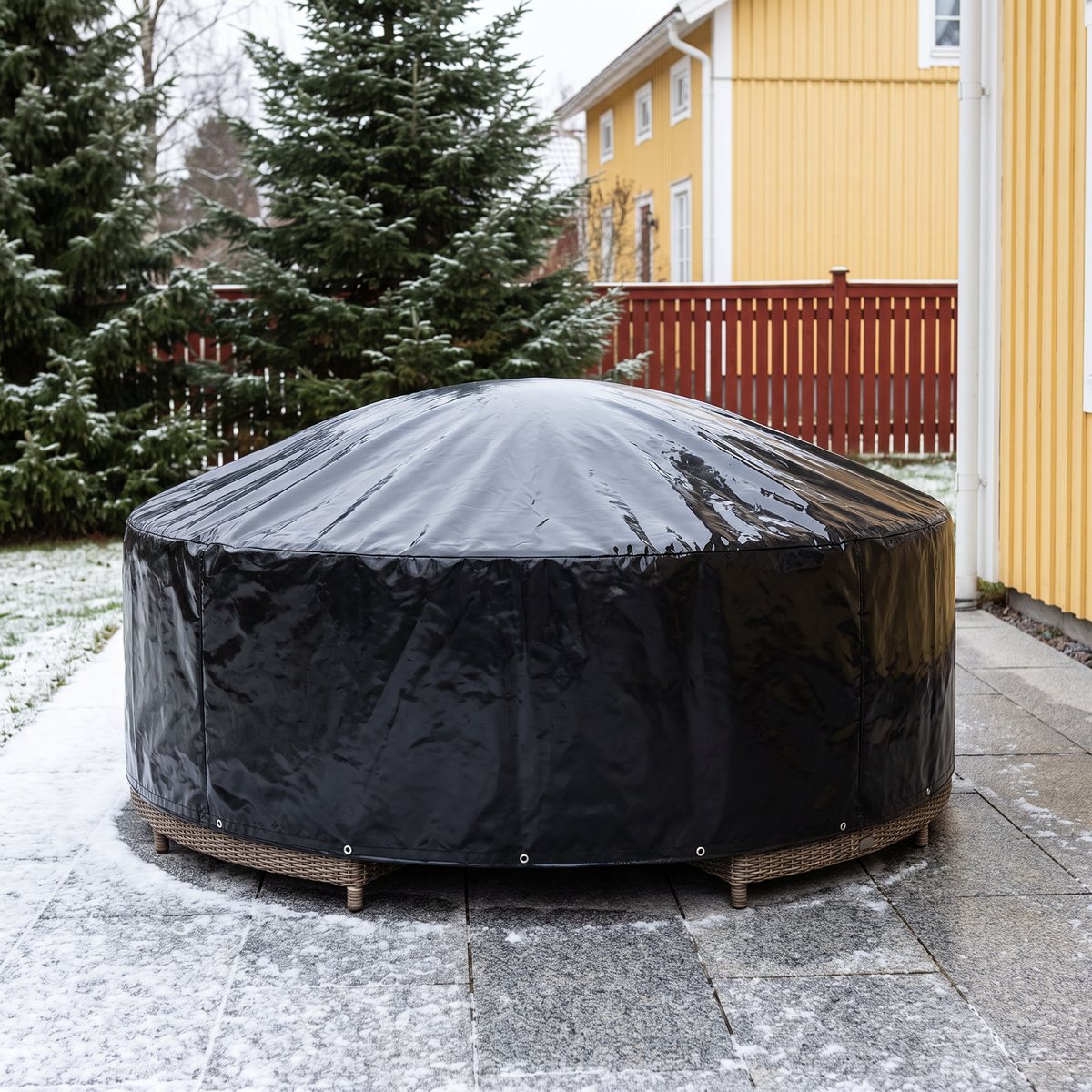 Runt, blankt svart vidaXL-överdrag över en rund rottinggrupp på en snöpudrad uteplats framför ett gult trähus