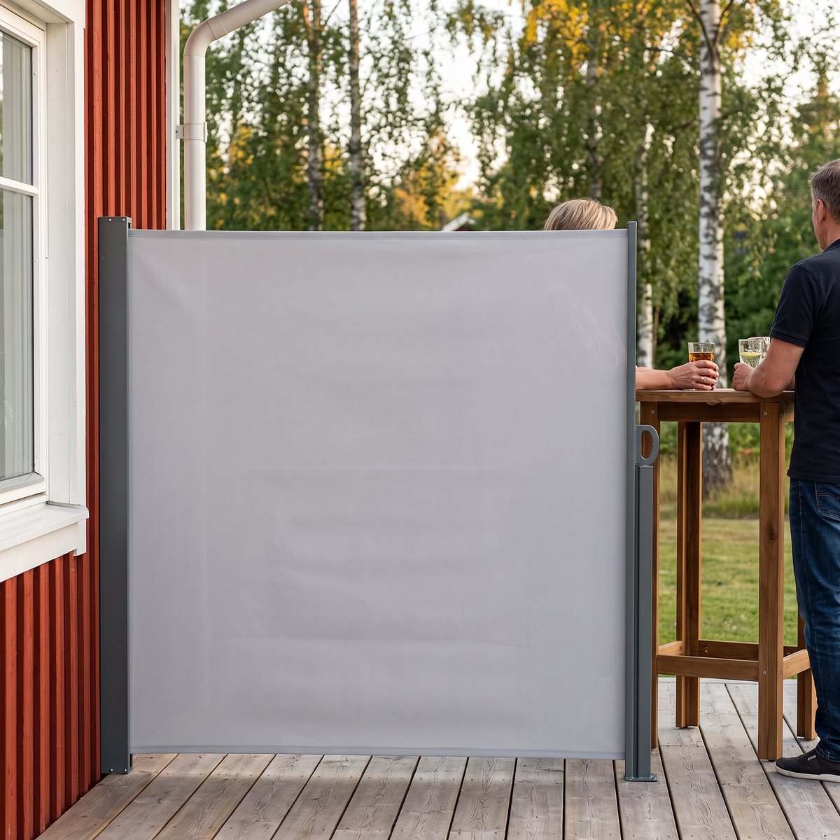 Ljusgrå sidomarkis utdragen från en kassett på husväggen vid en trätrall, två personer står vid ett högt bord i lä