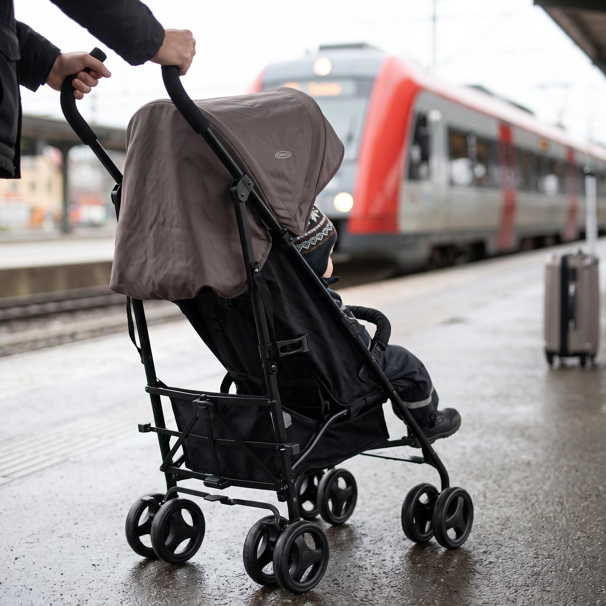 Graco TraveLite med barn på en svensk tågperron, förälder håller i båda handtagen