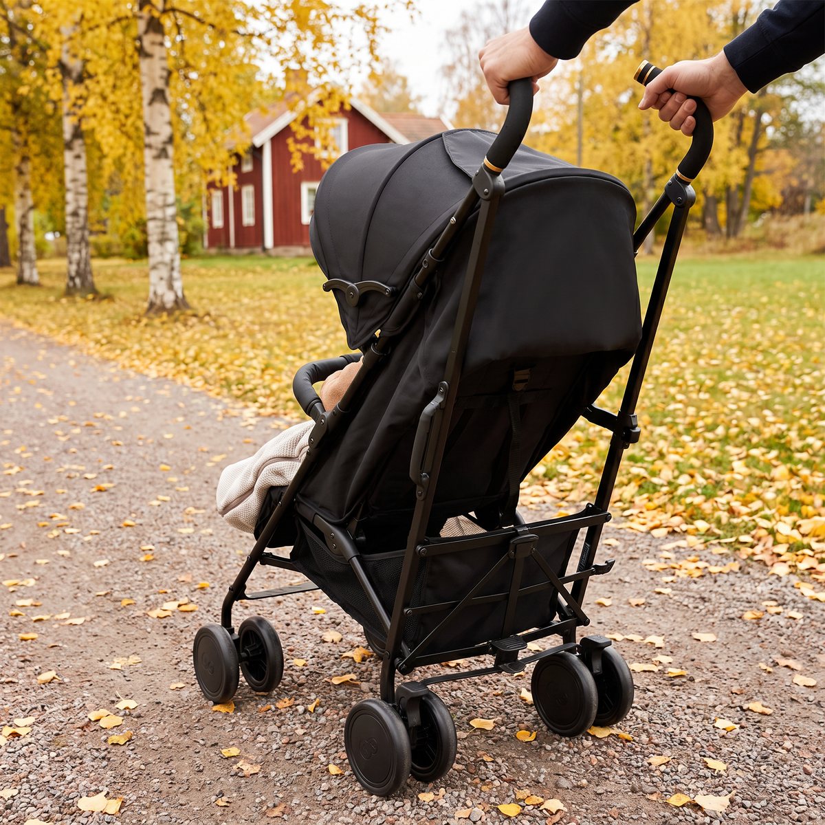 Svart Kinderkraft Siesta 2 med sovande barn under suffletten på en grusgång i en svensk höstpark