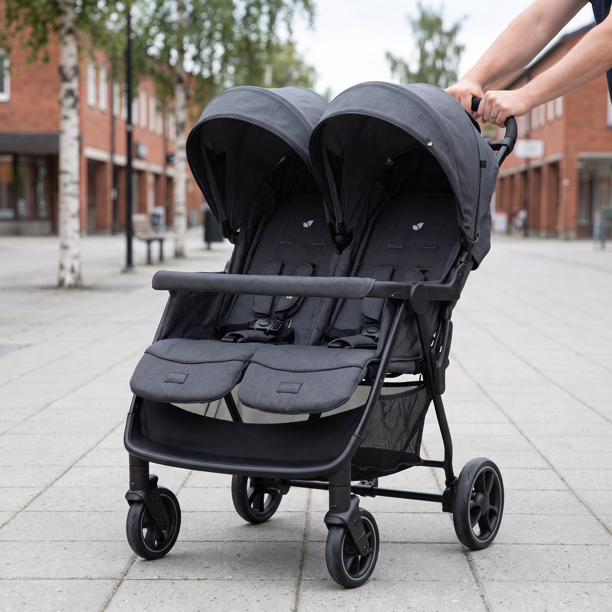 Joie Estrella i mörkgrått med två sittdelar bredvid varandra skjuts över betongplattor på ett torg i en svensk småstad