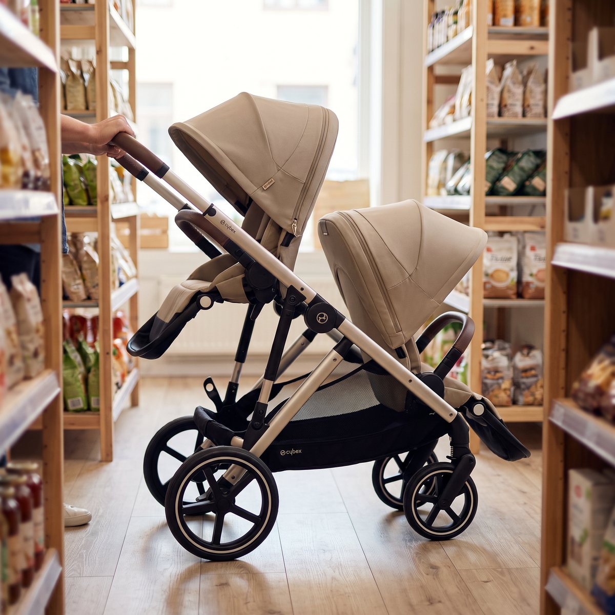 Beige Cybex Gazelle S med två sittdelar efter varandra skjuts mellan hyllorna i en liten svensk butik