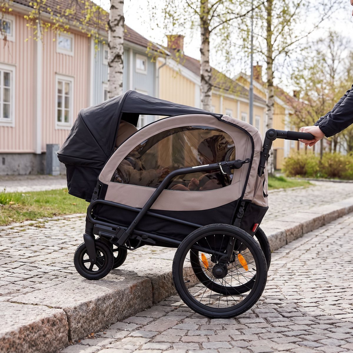 Beige Beemoo Activity Sport Lite som skjuts som barnvagn upp på en kantsten på en kullerstensgata i en svensk småstad.