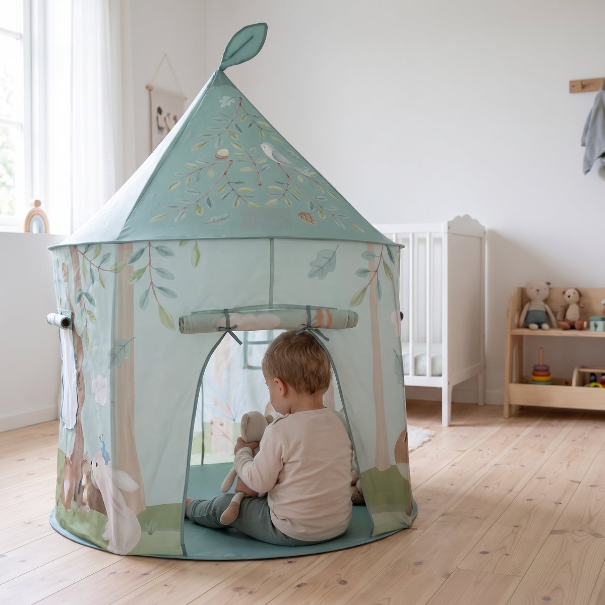 Runt mintgrönt torntält med skogsmotiv och spetsigt tak i ett svenskt barnrum, ett litet barn sitter i öppningen med ett mjukisdjur