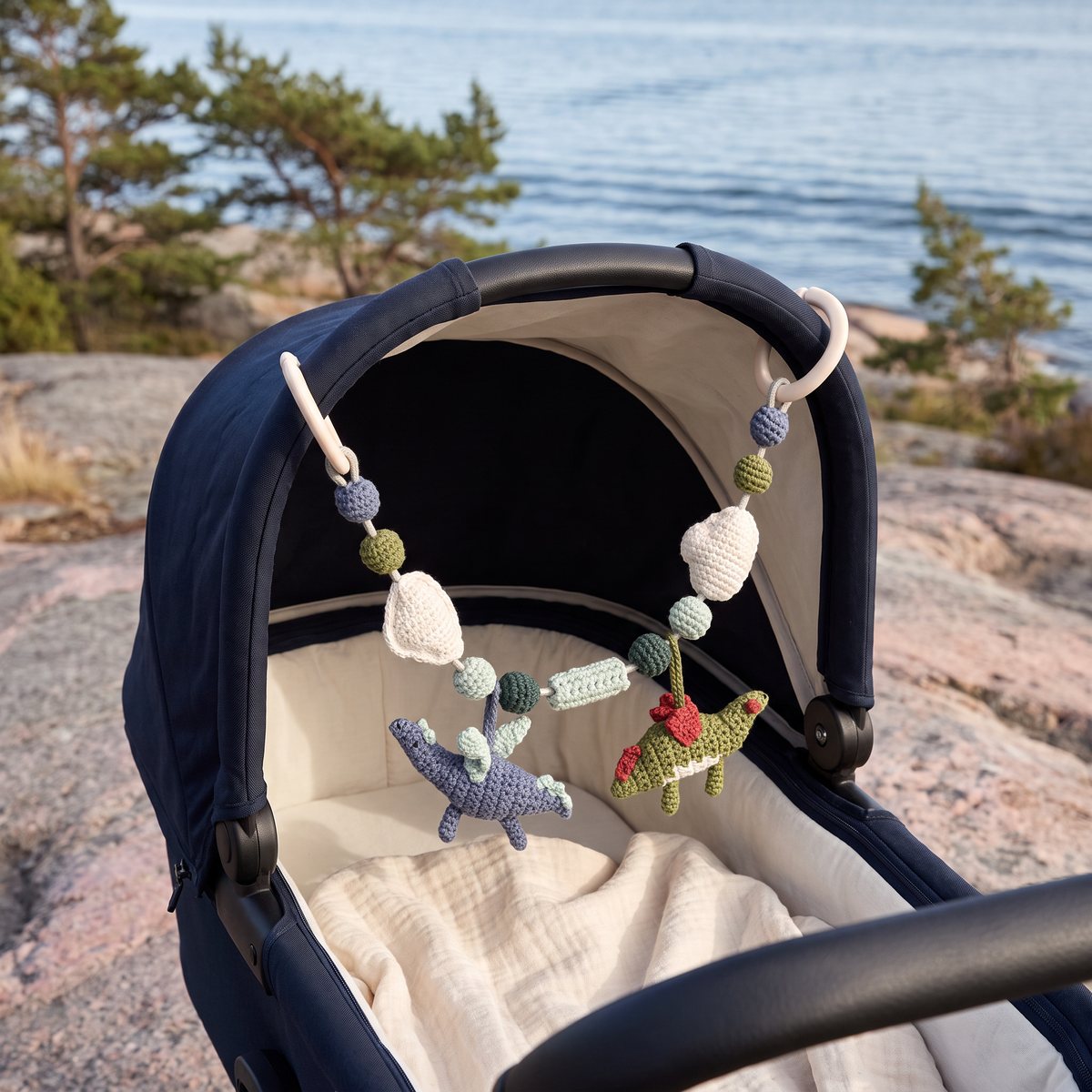 Sebras virkade drakhänge fäst med clips under suffletten på en mörkblå barnvagn på en granithäll vid havet i skärgården