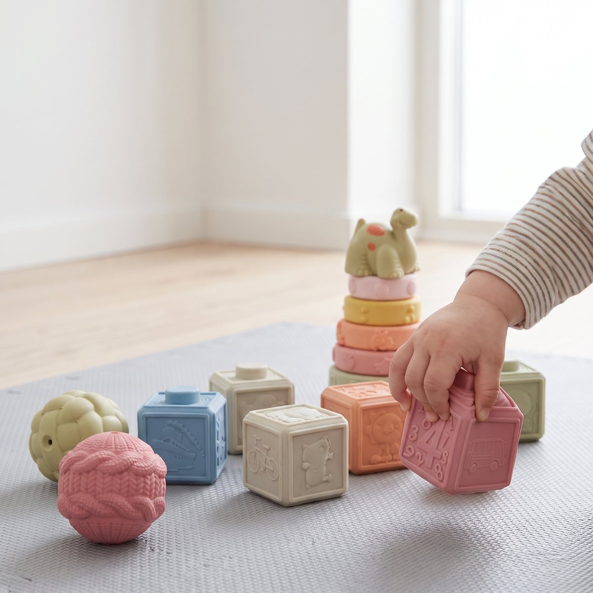 En babyhand klämmer en mjuk kloss ur Cloudberry Castles set på en lekmatta, med texturbollar och ringar bredvid