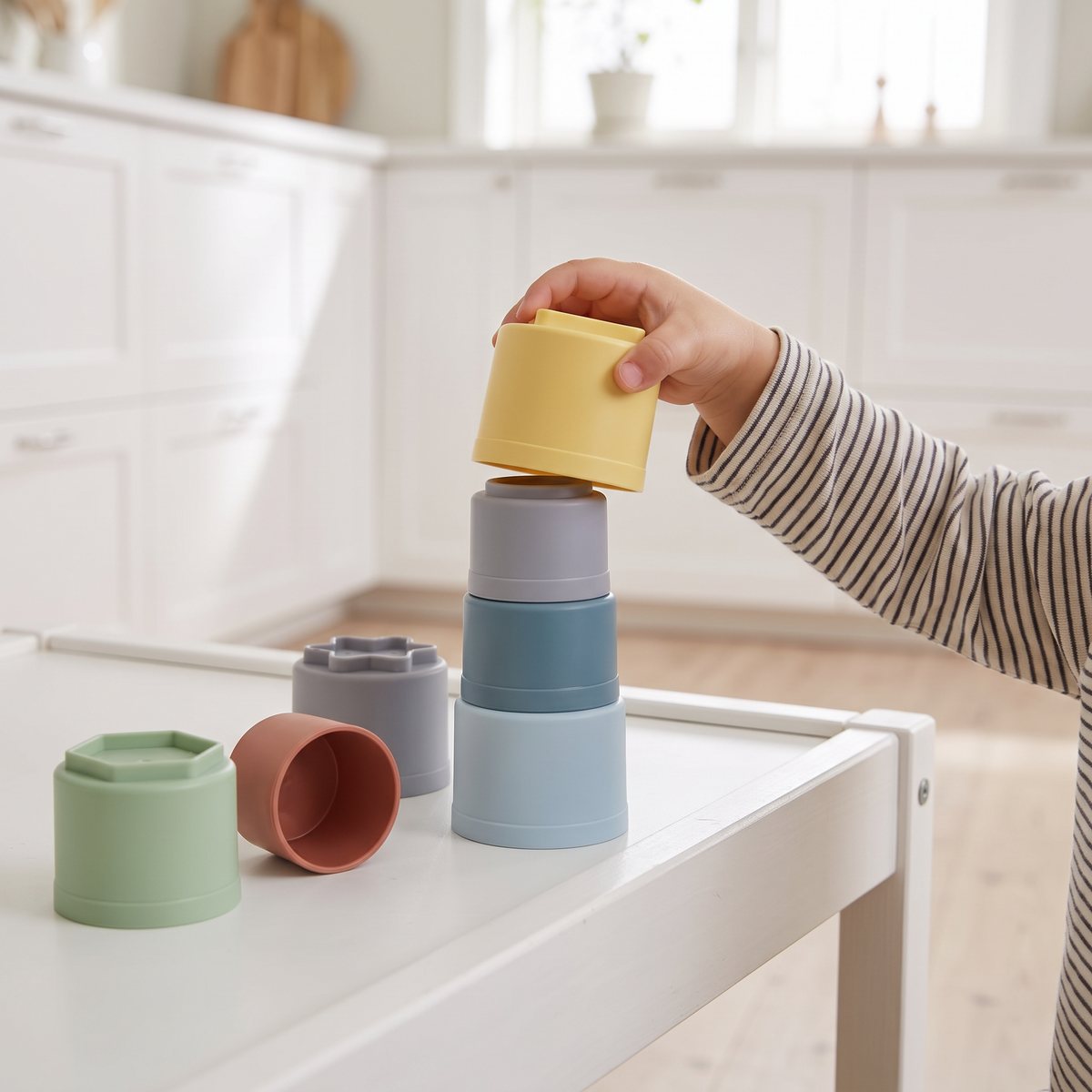En barnhand staplar Dantoys plastklossar i pastellfärger på ett vitt lekbord i ett ljust kök