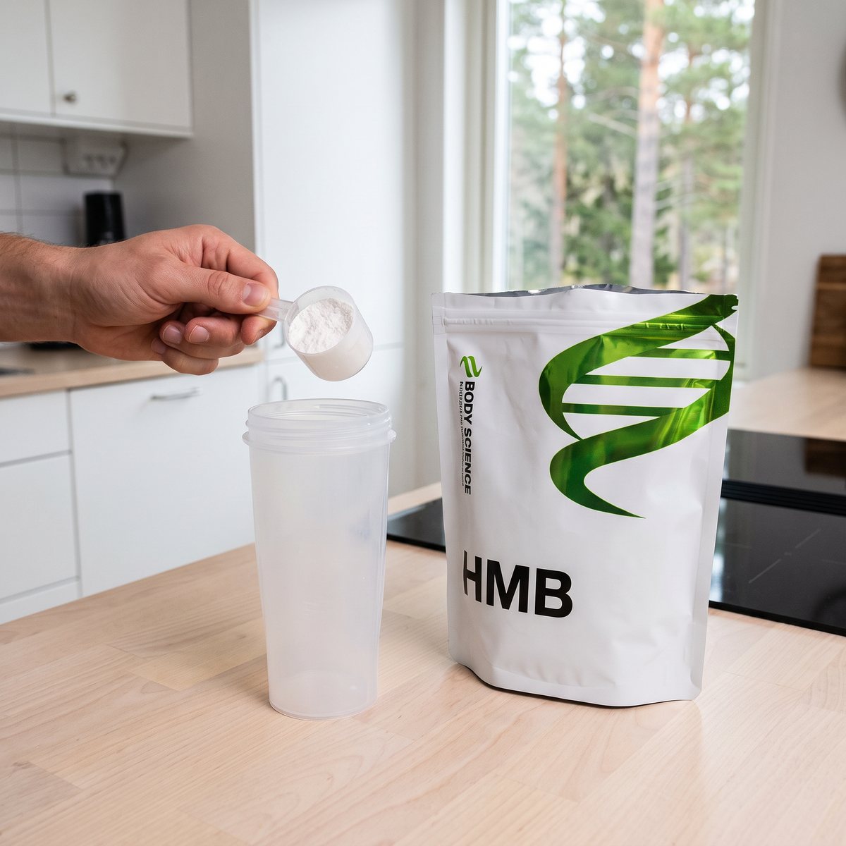 Body Science HMB-pulver i vit påse bredvid en shakerflaska när en hand tar en skopa pulver i ett ljust svenskt kök med induktionshäll och tallar utanför fönstret