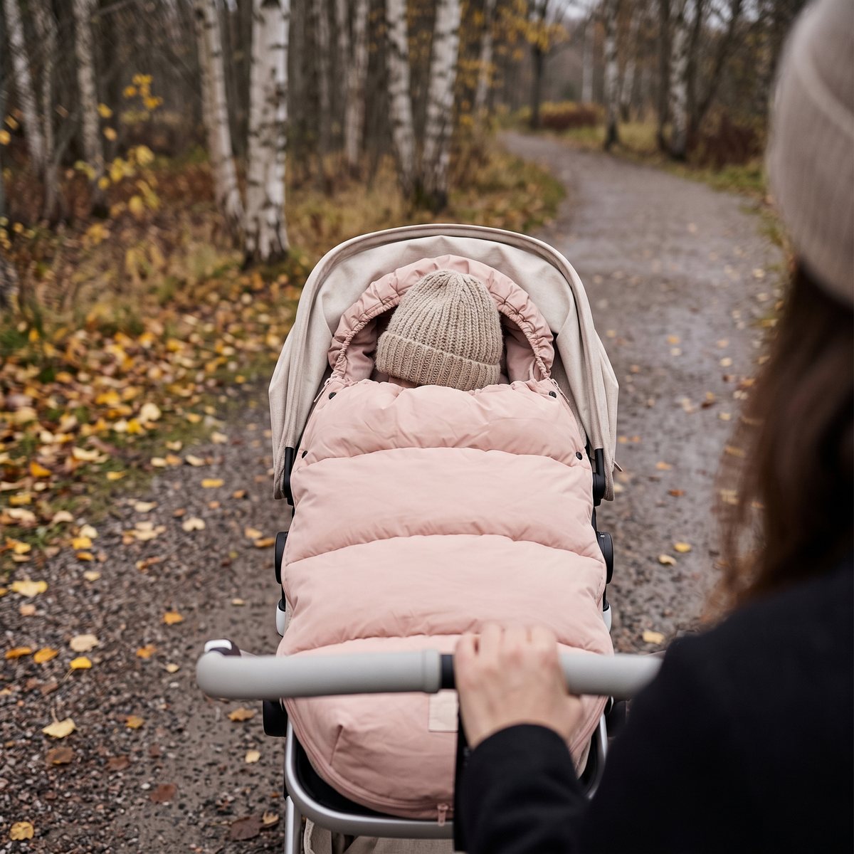 Rosa Elodie Details dunåkpåse med ett barn i mössa i en barnvagn på en grusväg bland björkar en höstdag