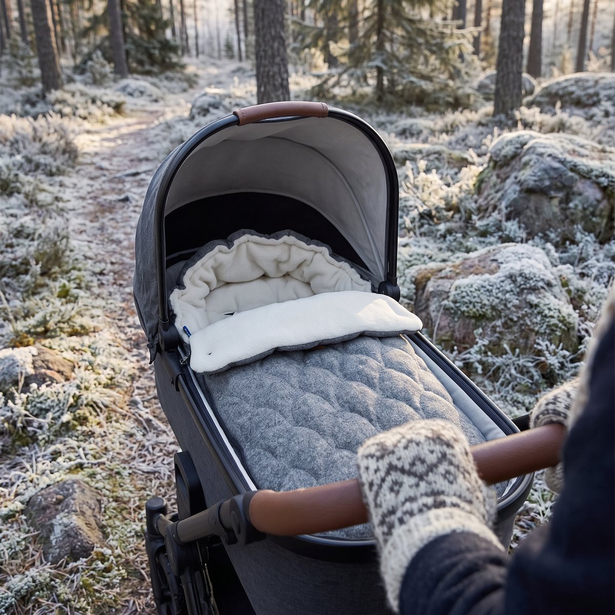 Grå Najell-åkpåse med vågmönster och vitt foder i en barnvagnsliggdel på en frostig skogsstig